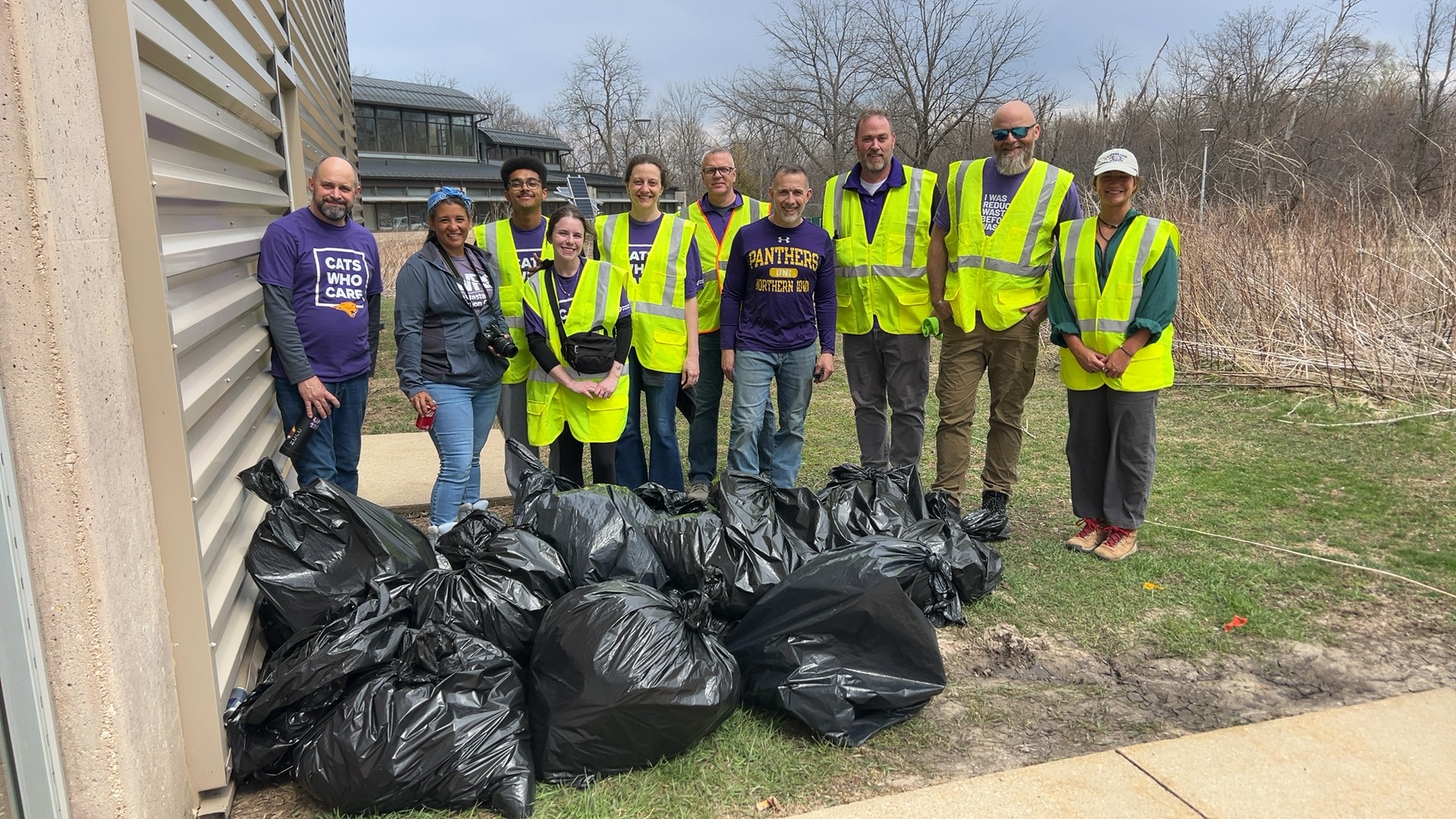 People in neon vest standing behind a pile of trash